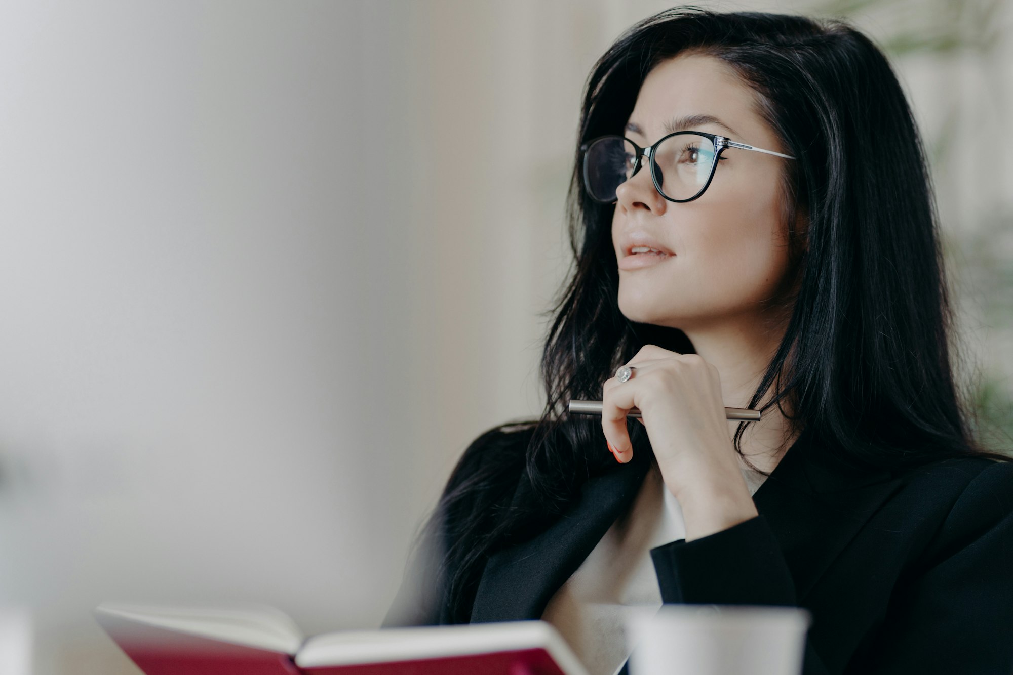 Thoughtful European woman makes notes in notepad, holds pen and writes down